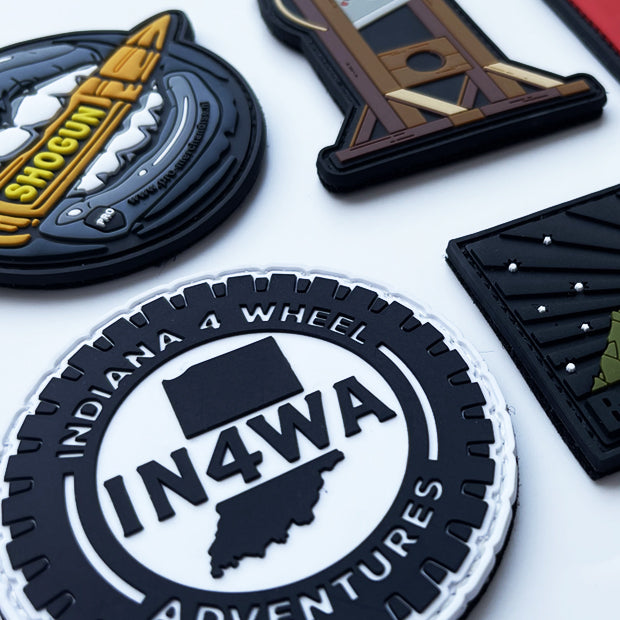 Close-up of custom rubber PVC die-cut patches featuring various company logos, embossed 3D designs, and intricate details, displayed on a white background.