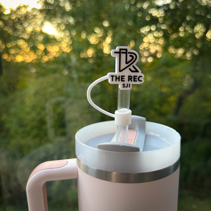 Custom rubber straw topper featuring The Rec SJI logo in black and white, made from soft PVC material, attached to a straw in a Stanley tumbler with a scenic outdoor background.